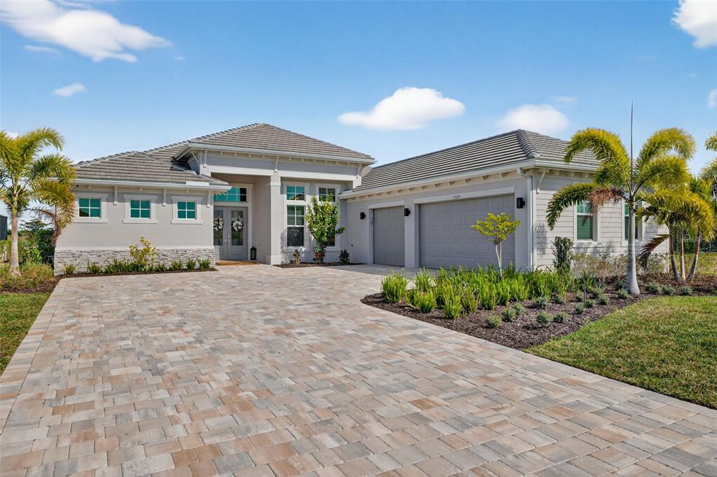 A single-story house with a paved driveway, gray exterior, and palm trees under a blue sky — 17395 BLUE SAPPHIRE DRIVE, FORT MYERS, FL