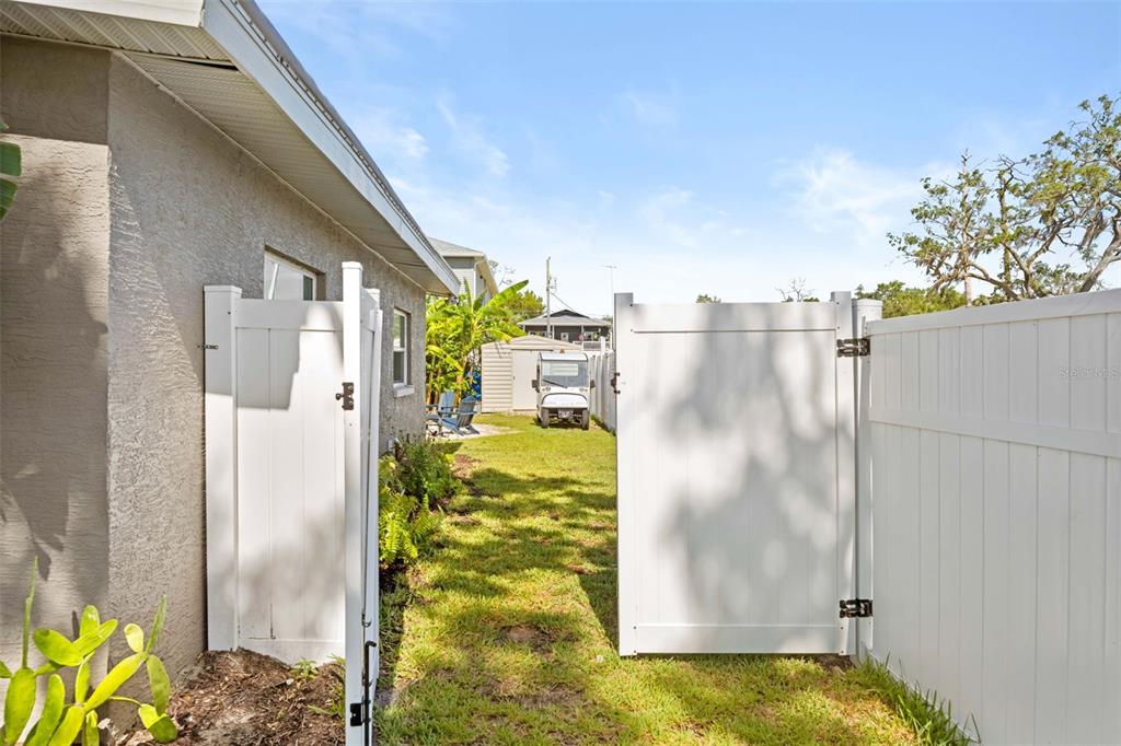 A view through an open white vinyl gate into a grassy backyard with a shed — 5041 MAPLEWOOD, HERNANDO BEACH, FL