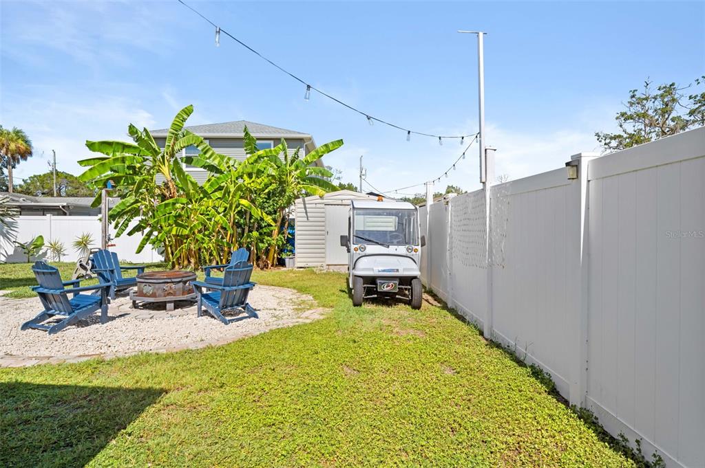 A backyard features a gravel patio with blue chairs, a fire pit, and a golf cart — 5041 MAPLEWOOD, HERNANDO BEACH, FL