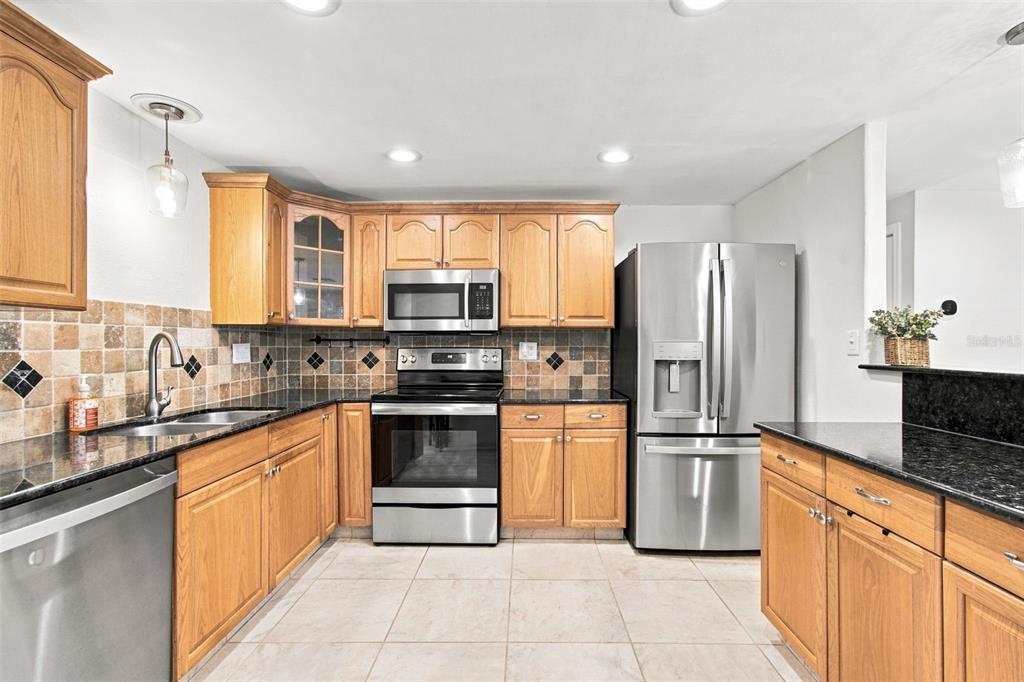 A kitchen with light wood cabinets, stainless steel appliances, dark countertops, and a tiled backsplash — 8467 77TH AVENUE, SEMINOLE, FL
