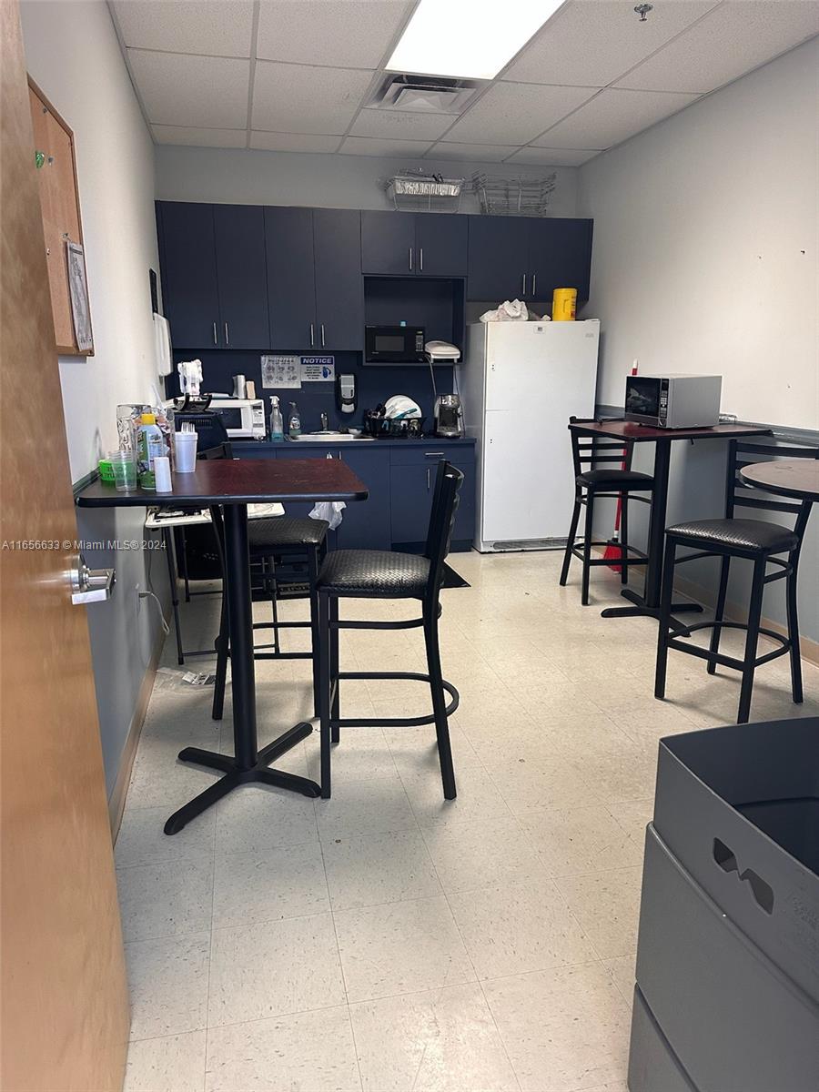 A breakroom features dark blue cabinetry, a white refrigerator, two high-top tables, and chairs — FORT LAUDERDALE, FL
