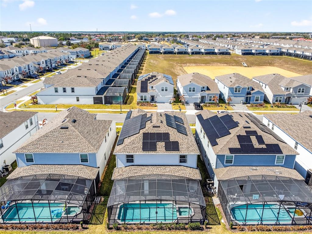 An aerial view shows three suburban houses with screened-in pools and rooftop solar panels — 3711 LANA AVENUE, DAVENPORT, FL
