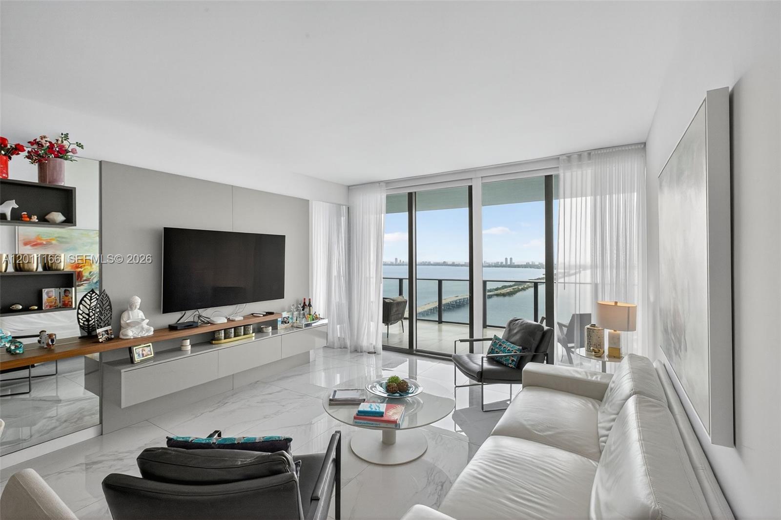 A modern living room features white marble floors, a wall-mounted television, and a balcony view — 3131 NE 7th Ave # 4503, Miami FL 33137, MIAMI, FL