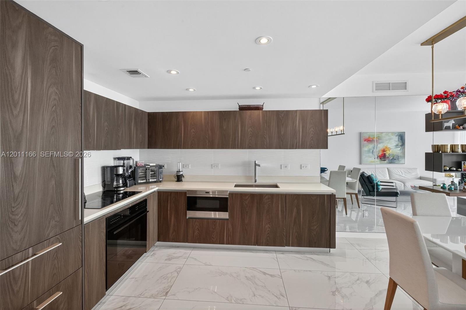 A modern kitchen features dark wood cabinetry, white countertops, and white marble tile flooring — 3131 NE 7th Ave # 4503, Miami FL 33137, MIAMI, FL