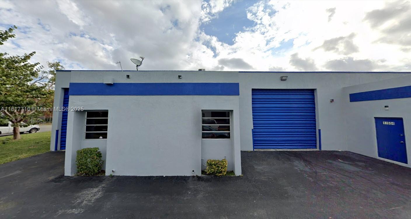 An exterior view of a single-story commercial building with blue trim and a roll-up door — 13552 SW 129th St, Miami FL 33186, MIAMI, FL