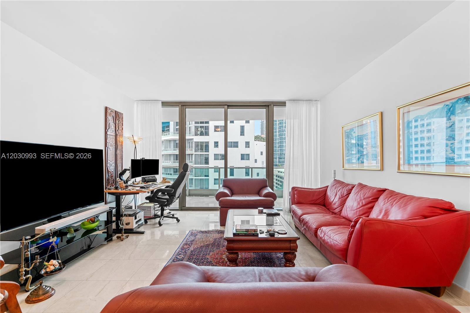 A living room features red leather sofas, a coffee table, and a desk near a balcony — 1331 BRICKELL BAY DR # 1004, Miami FL 33131, MIAMI, FL