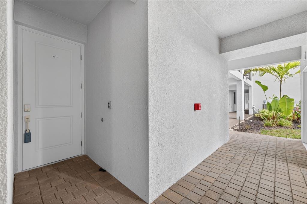 A white front door with a lockbox opens onto a paved walkway near tropical landscaping — 14201 HERITAGE LANDING BOULEVARD UNIT 1312, PUNTA GORDA, FL