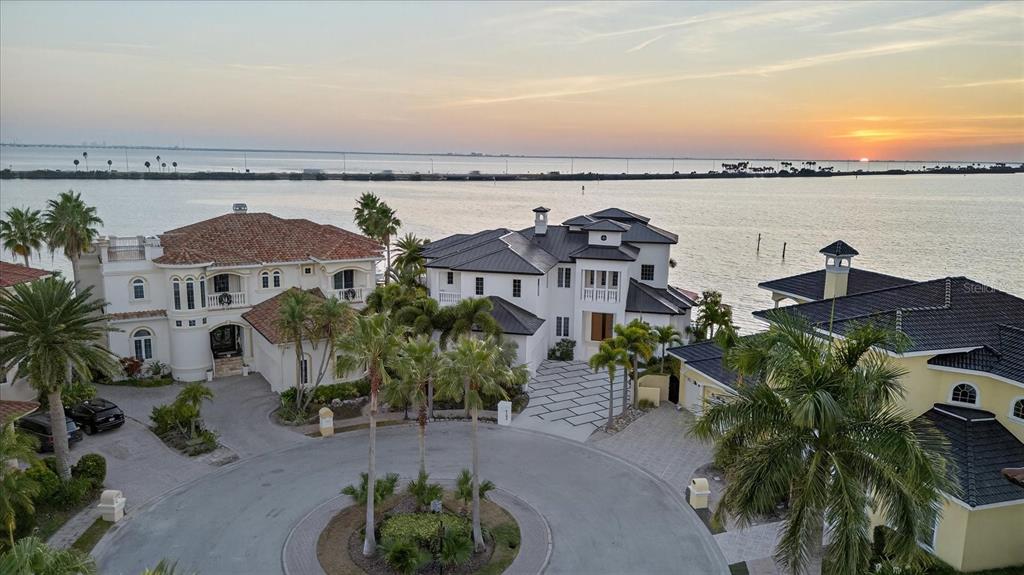 An aerial view shows three large waterfront houses situated around a circular driveway at sunset — 4102 CAUSEWAY VISTA DRIVE, TAMPA, FL