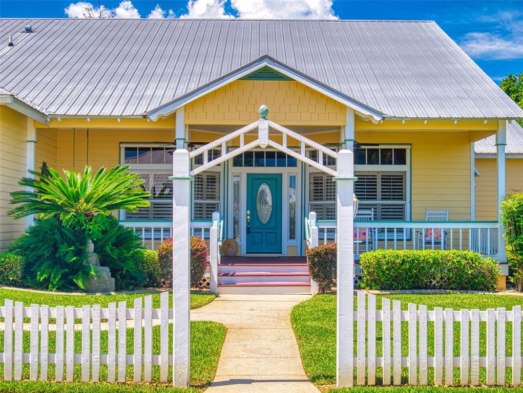 A yellow house with a metal roof, white picket fence, and a teal front door — 2815 BAY SIDE DRIVE, NEW SMYRNA BEACH, FL