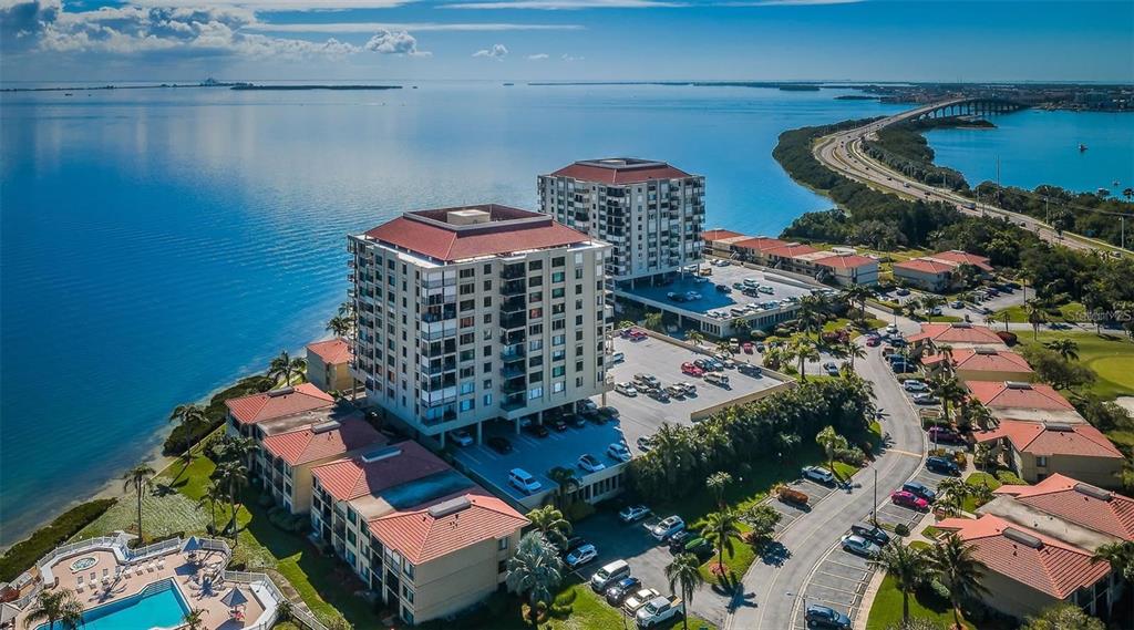 An aerial view shows two multi-story residential buildings situated along a waterfront with a bridge nearby — 6322 PALMA DEL MAR BLVD S UNIT 103, ST PETERSBURG, FL