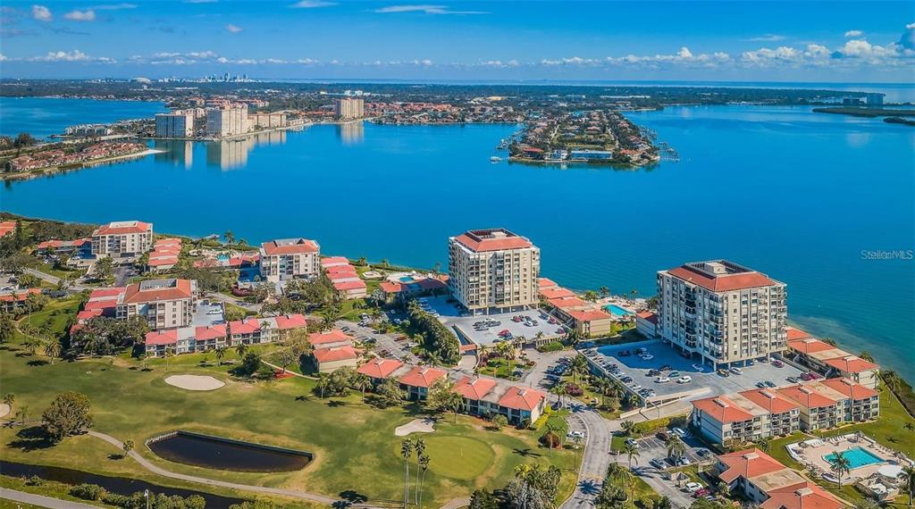 An aerial view of a waterfront condominium complex featuring multiple buildings, parking lots, and landscaping — 6322 PALMA DEL MAR BLVD S UNIT 103, ST PETERSBURG, FL