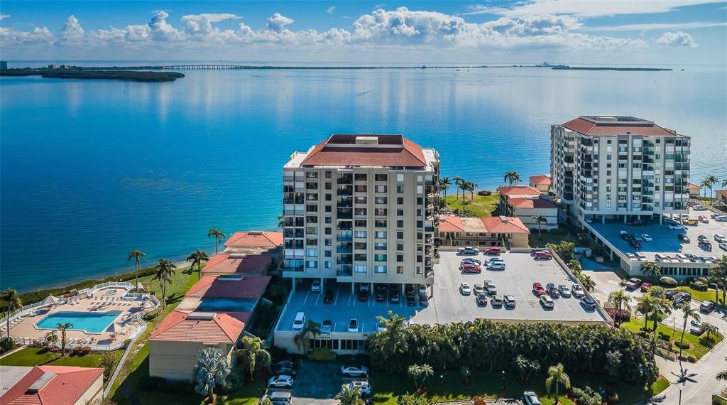 An aerial view shows two multi-story apartment buildings with parking lots next to the ocean — 6322 PALMA DEL MAR BLVD S UNIT 103, ST PETERSBURG, FL