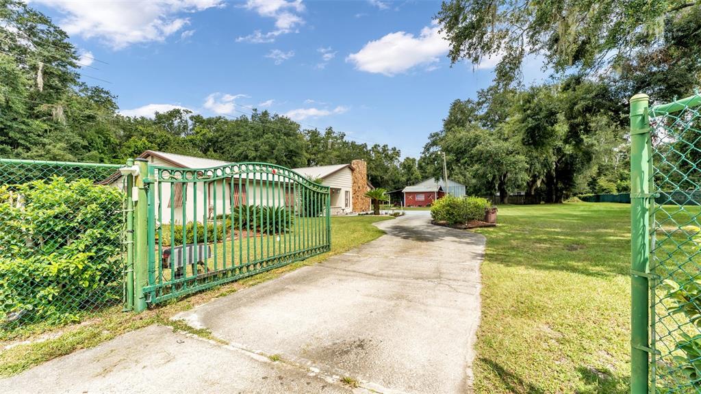 A concrete driveway leads through a green metal gate toward a house and small shed — 1301 LANIER ROAD, LAKELAND, FL