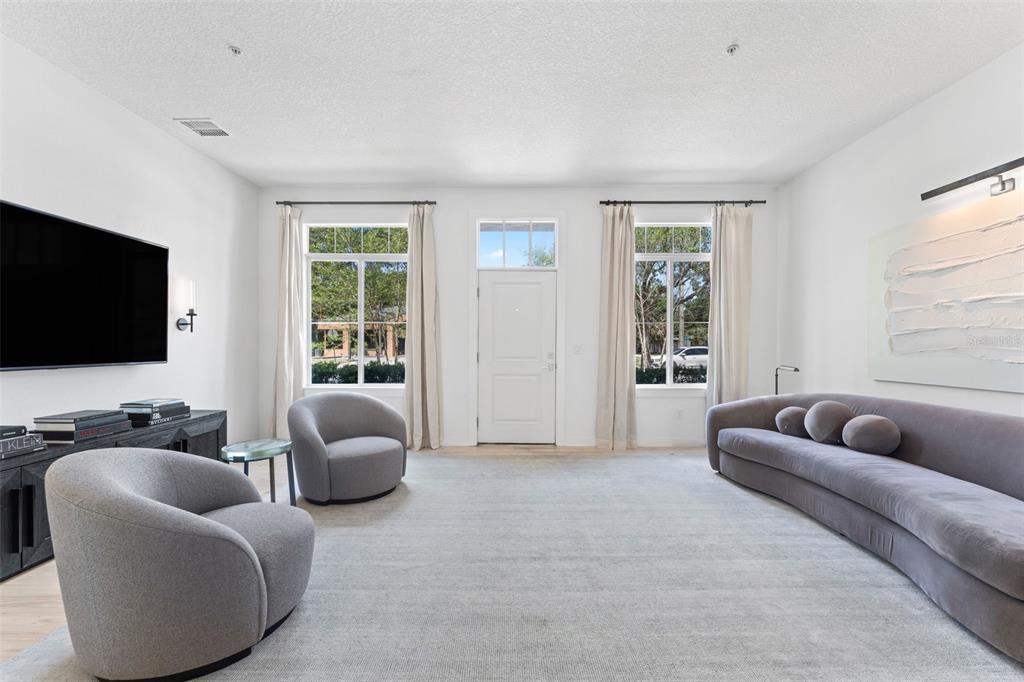 A modern living room features a curved sofa, two gray armchairs, and a wall-mounted television — 771 LAKE BALDWIN LANE, ORLANDO, FL