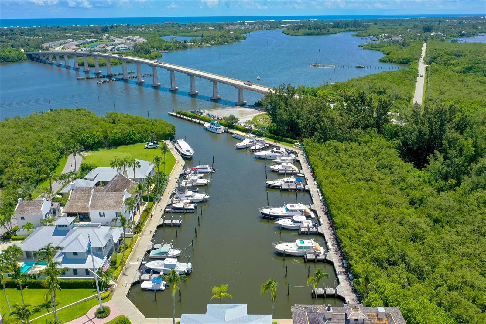 An aerial view shows a marina with docked boats next to waterfront houses and a bridge — 9260 E Marsh Island Drive, Vero Beach FL 32963, VERO BEACH, FL