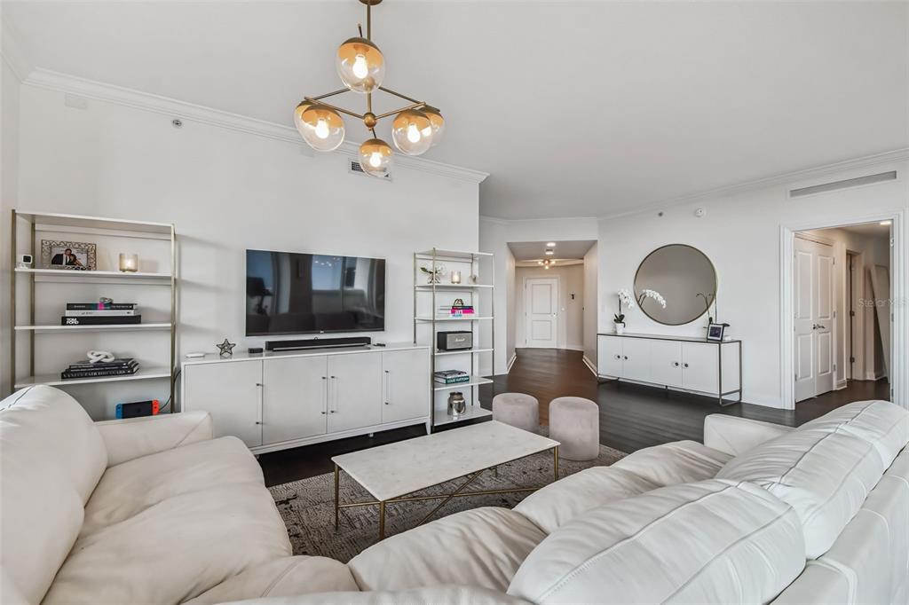 A modern living room features a white sectional sofa, a television console, and a chandelier — 450 KNIGHTS RUN AVENUE UNIT 502, TAMPA, FL