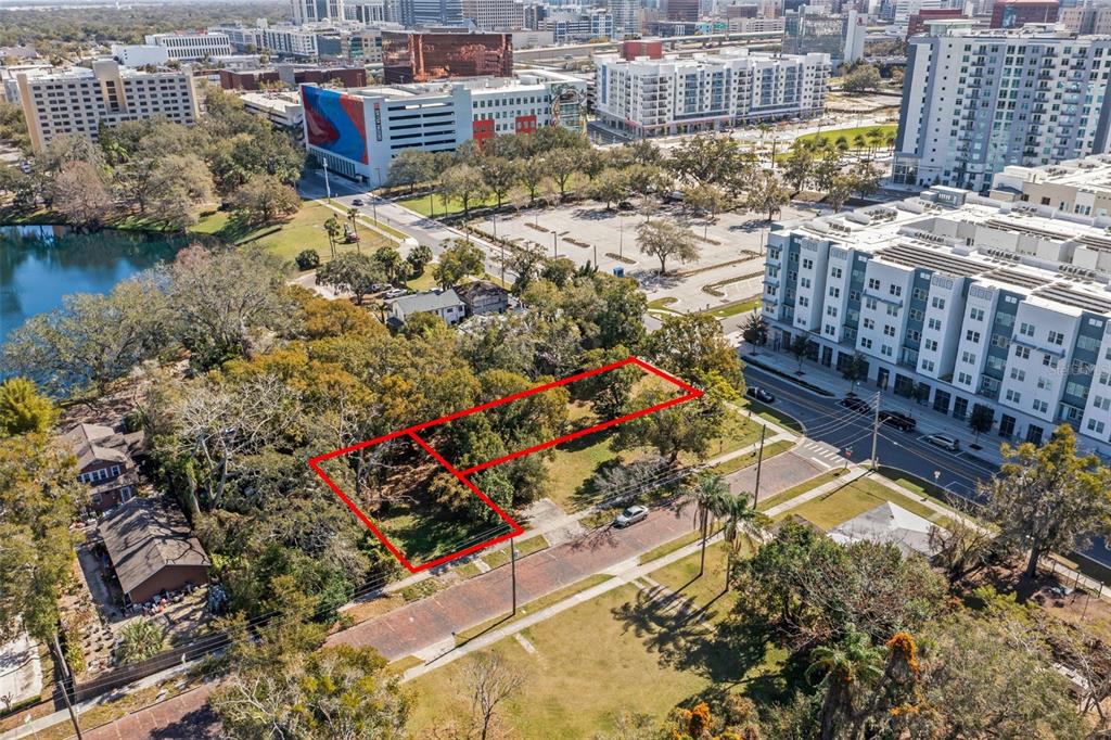 An aerial view shows a vacant, tree-covered rectangular lot outlined in red near city buildings — 623 W CONCORD STREET, ORLANDO, FL