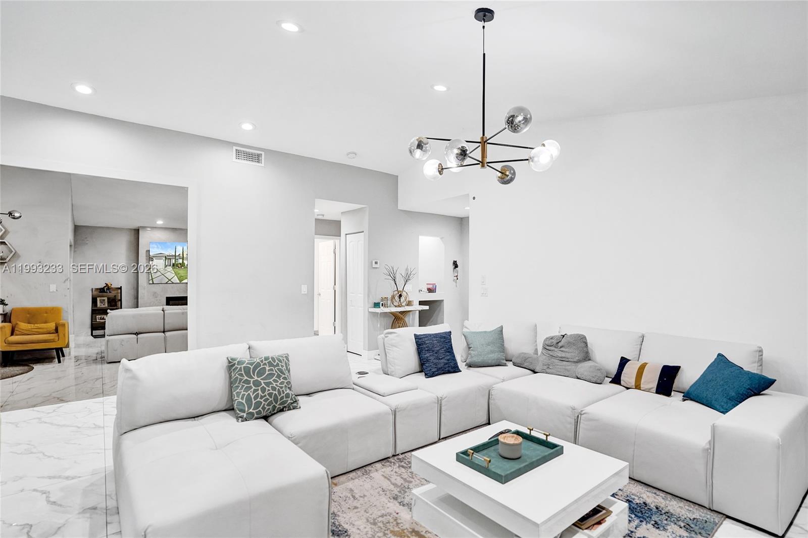 A modern living room features a large white sectional sofa, a coffee table, and a chandelier — 372 W Riverbend Dr, Sunrise FL 33326, SUNRISE, FL