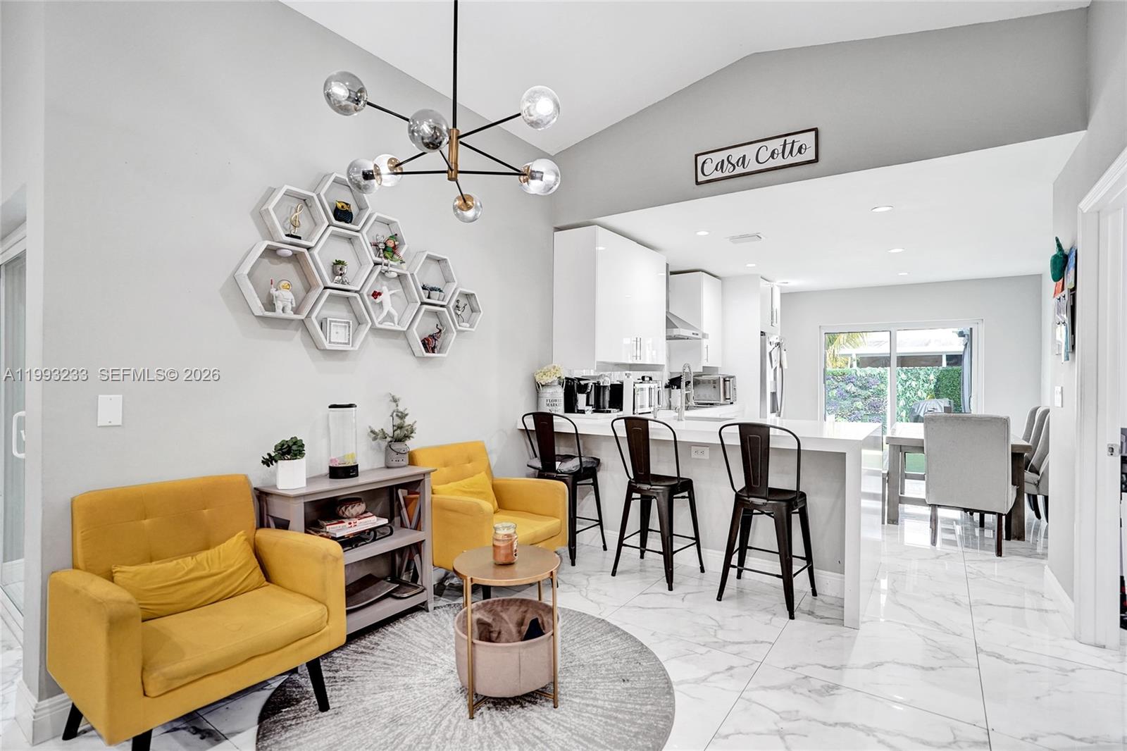 A modern living room and kitchen area features yellow armchairs, hexagon wall shelves, and stools — 372 W Riverbend Dr, Sunrise FL 33326, SUNRISE, FL