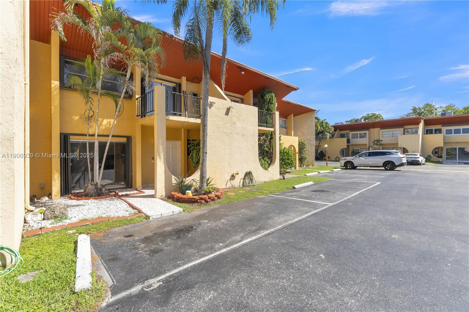 A two-story yellow apartment building features balconies, palm trees, and an adjacent parking lot — 13715 SW 84th St # F, Miami FL 33183, MIAMI, FL