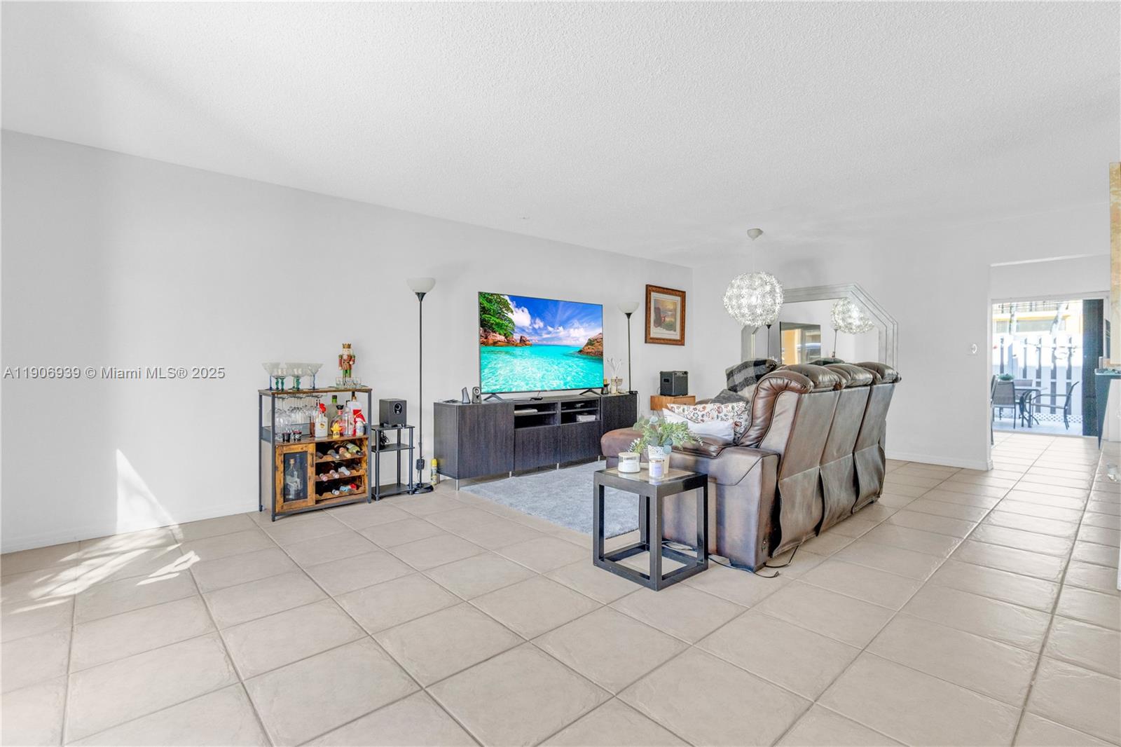 A living room features tile flooring, a brown leather sofa, and a wall-mounted television — 13715 SW 84th St # F, Miami FL 33183, MIAMI, FL