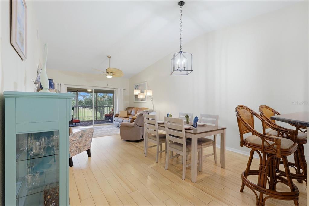 An open-concept dining and living area features light wood flooring, a dining set, and balcony access — 5725 GREENWOOD AVENUE UNIT 7203, NORTH PORT, FL