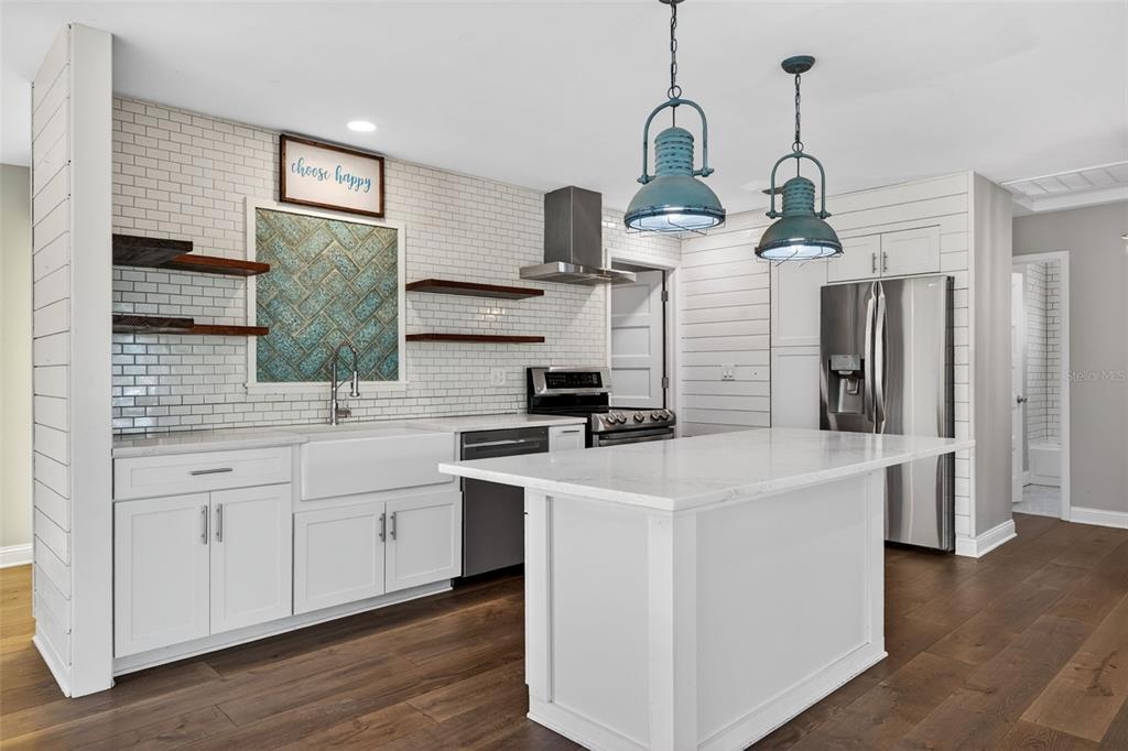 A modern kitchen features white cabinetry, a marble-topped island, subway tile backsplash, and open shelving — 4200 BEACH DRIVE SE, ST PETERSBURG, FL