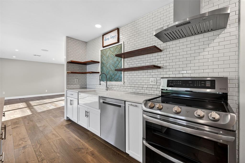 A kitchen features white cabinets, a farmhouse sink, subway tile backsplash, and wood floating shelves — 4200 BEACH DRIVE SE, ST PETERSBURG, FL