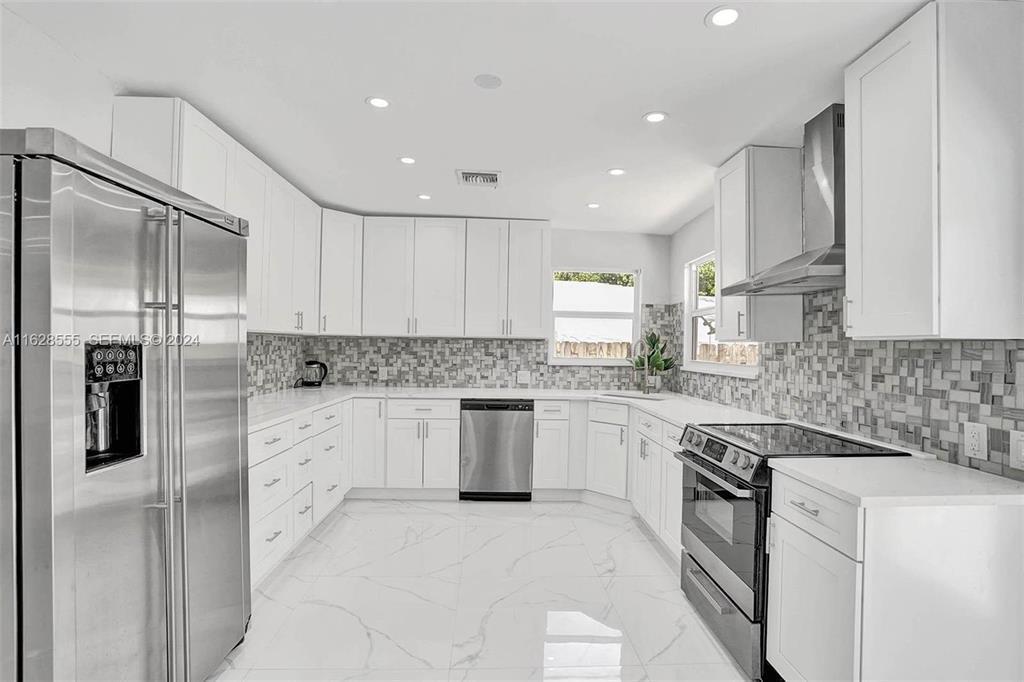 A modern kitchen features white cabinetry, stainless steel appliances, and a gray mosaic tile backsplash — 3421 Dover Road, Pompano Beach FL 33062, POMPANO BEACH, FL