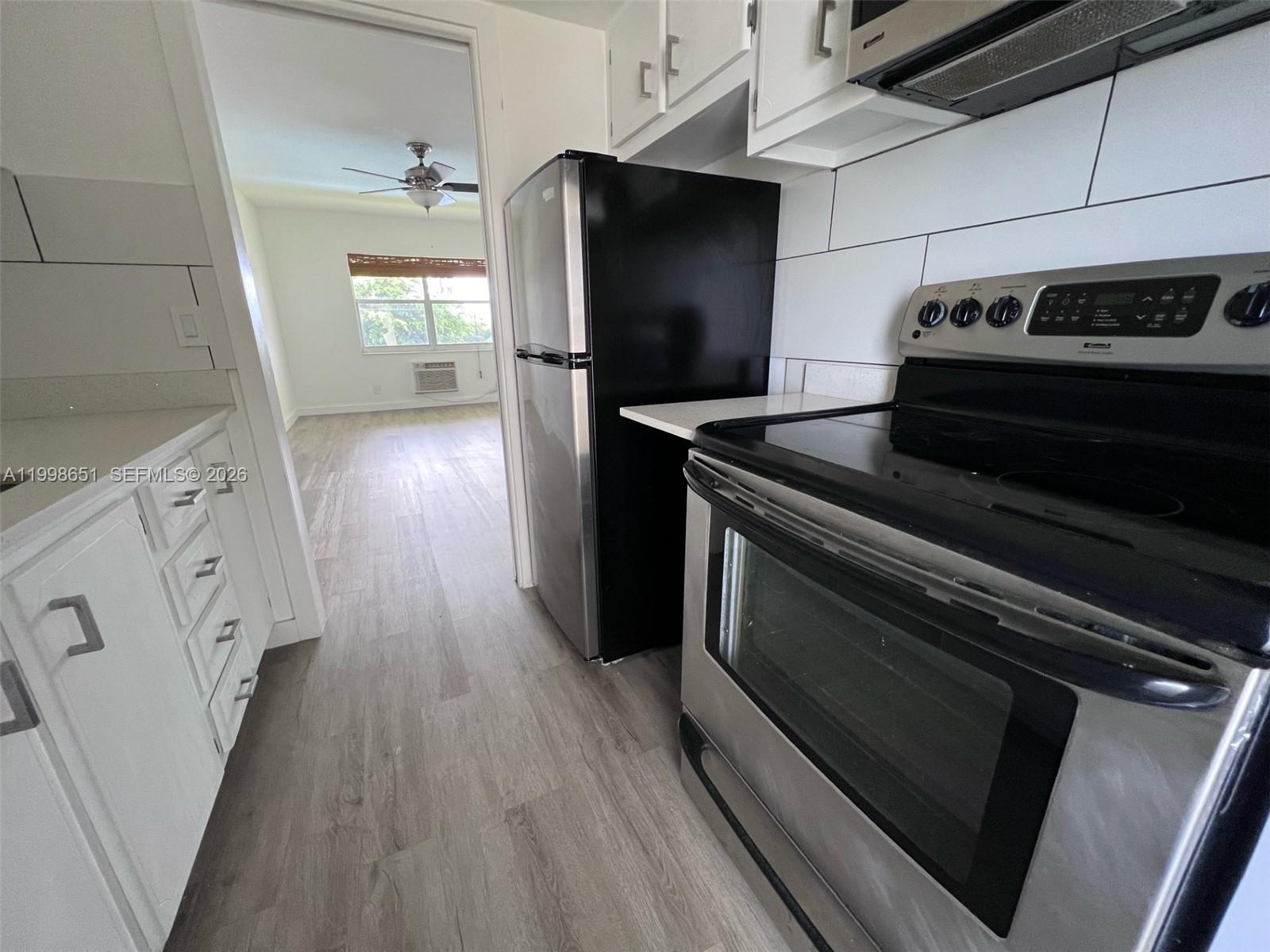 A kitchen with stainless steel appliances and white cabinets leads into a living area — 1350 E Sample Rd # 306, Pompano Beach FL 33064, POMPANO BEACH, FL
