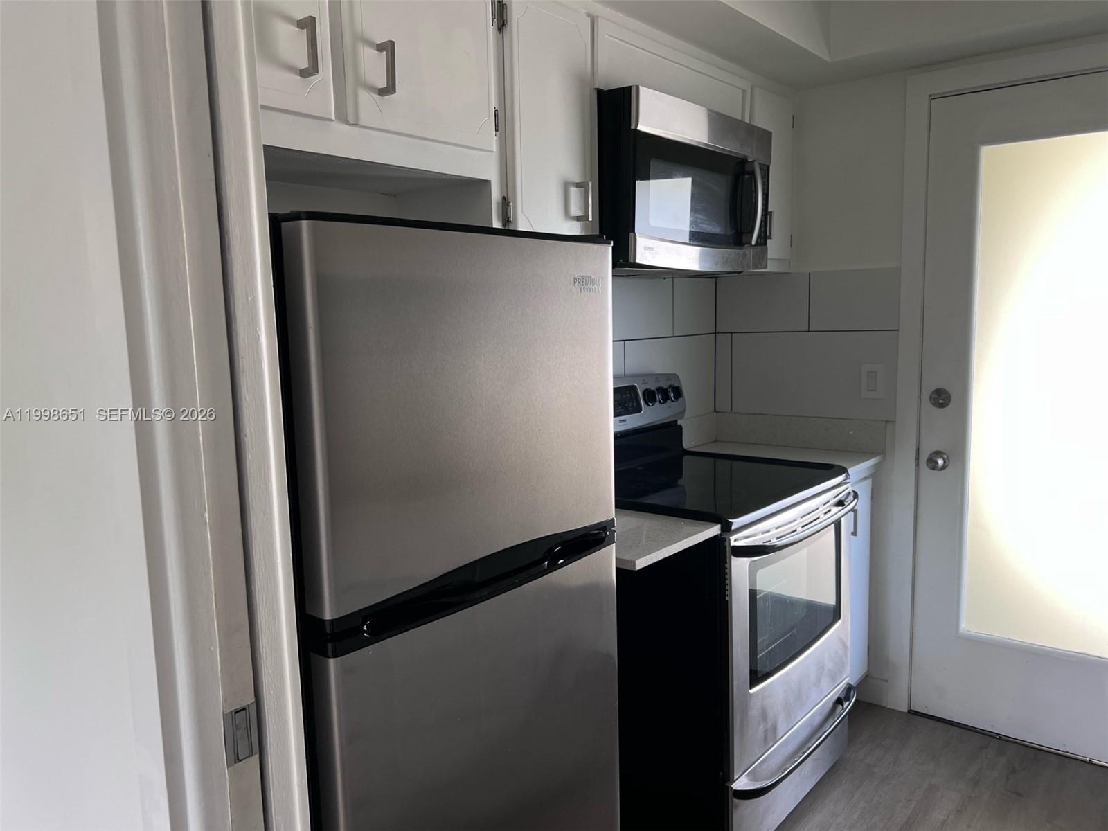 A kitchen features stainless steel appliances, white cabinets, and a glass-paneled exterior door — 1350 E Sample Rd # 306, Pompano Beach FL 33064, POMPANO BEACH, FL