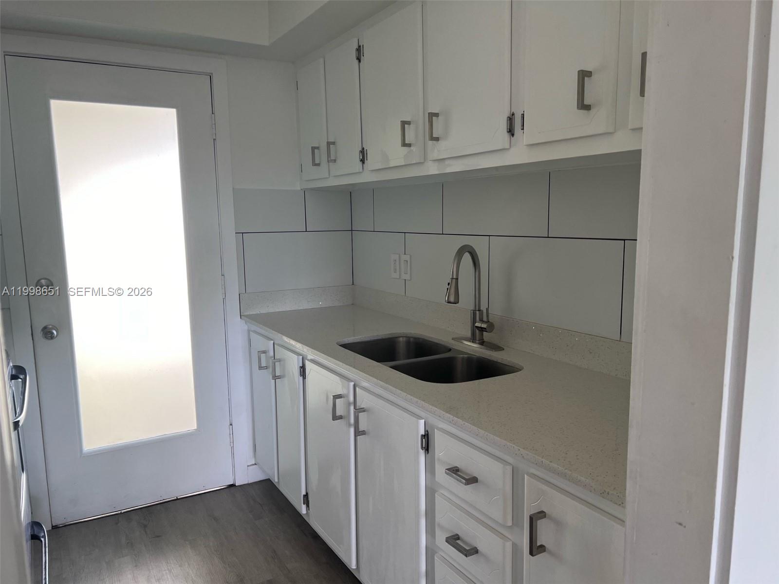 A kitchen features white cabinets, a light-colored countertop, a double sink, and white backsplash tiles — 1350 E Sample Rd # 306, Pompano Beach FL 33064, POMPANO BEACH, FL