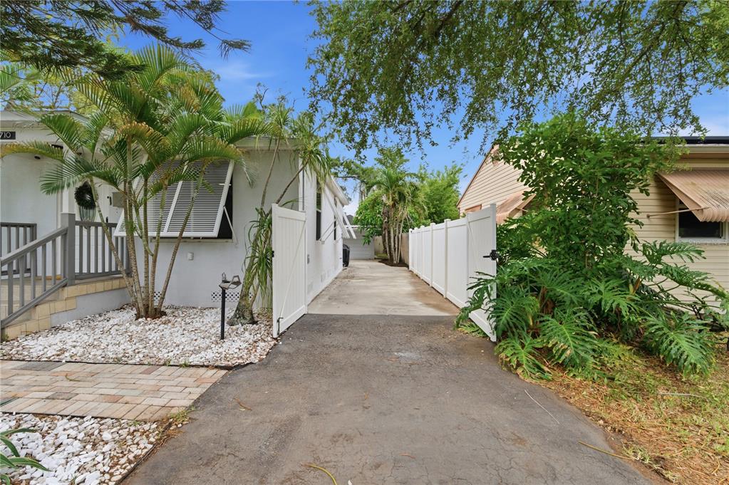 A paved driveway leads between two houses toward a detached garage behind a white fence — 2710 16TH AVENUE N, ST PETERSBURG, FL