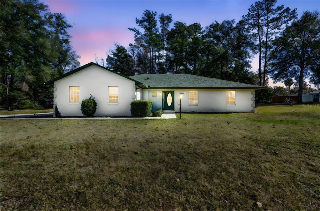 A single-story white house with a green roof and front door sits on a lawn — 12681 SE 54TH AVENUE, BELLEVIEW, FL