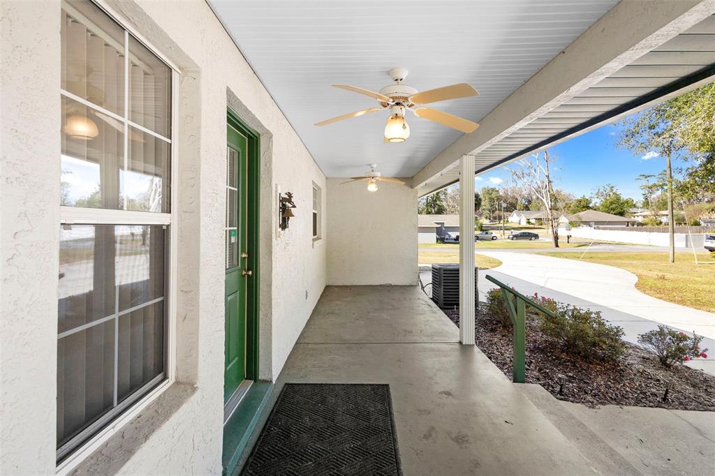 A covered concrete porch features a green door, two ceiling fans, and a railing — 12681 SE 54TH AVENUE, BELLEVIEW, FL