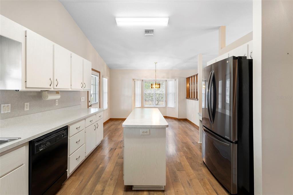 A kitchen with white cabinets, a central island, and stainless steel appliances on wood flooring — 12681 SE 54TH AVENUE, BELLEVIEW, FL