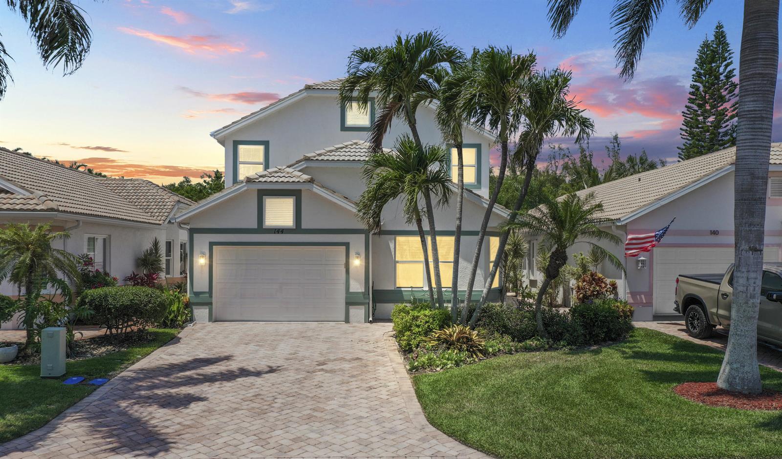 A two-story house with a paved driveway, palm trees, and a garage at sunset — 144 Pepper Lane, Jensen Beach FL 34957, JENSEN BEACH, FL