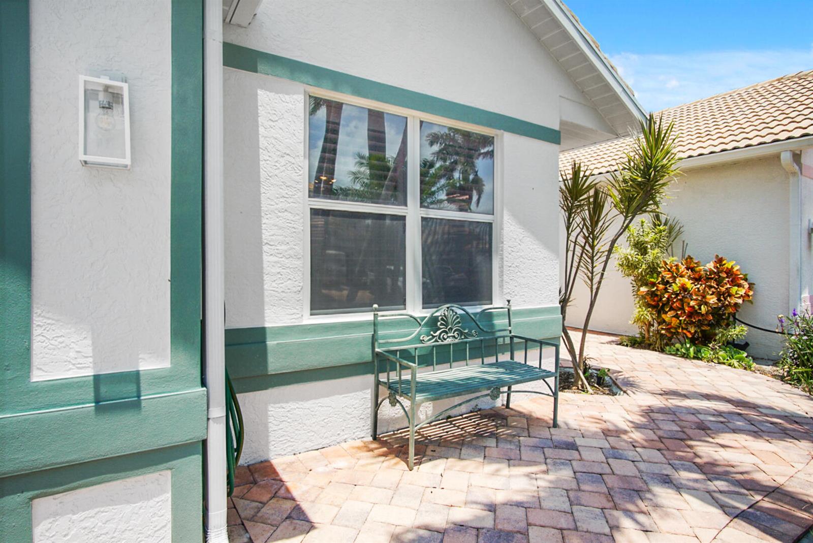 A green metal bench sits on a brick patio in front of a white house — 144 Pepper Lane, Jensen Beach FL 34957, JENSEN BEACH, FL