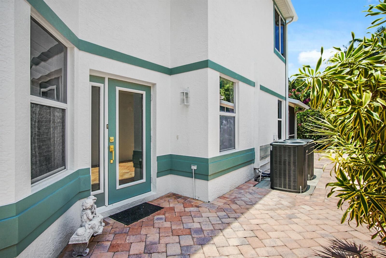 A white house exterior features teal trim, a glass door, and a brick patio — 144 Pepper Lane, Jensen Beach FL 34957, JENSEN BEACH, FL