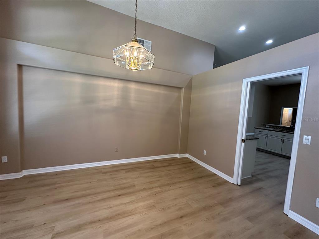 An empty dining room features light wood-look flooring, tan walls, and a brass chandelier — 13813 BLUEWATER CIRCLE, ORLANDO, FL