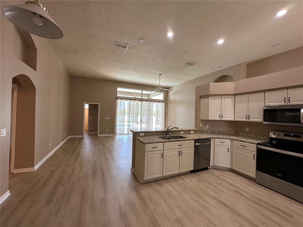 An open-concept kitchen with light-colored cabinets and granite countertops overlooks a spacious living area — 13813 BLUEWATER CIRCLE, ORLANDO, FL