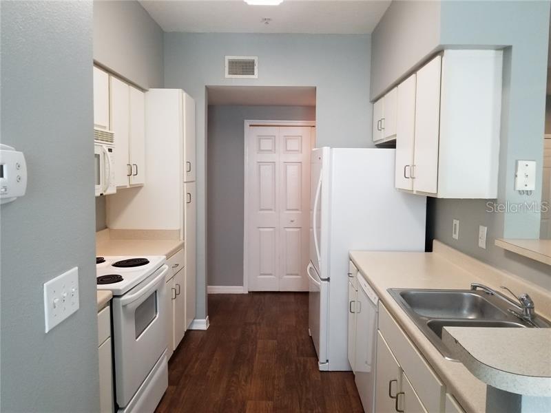 A galley-style kitchen features white cabinets, laminate countertops, and wood-look flooring — 1810 E PALM AVE UNIT 6204, TAMPA, FL