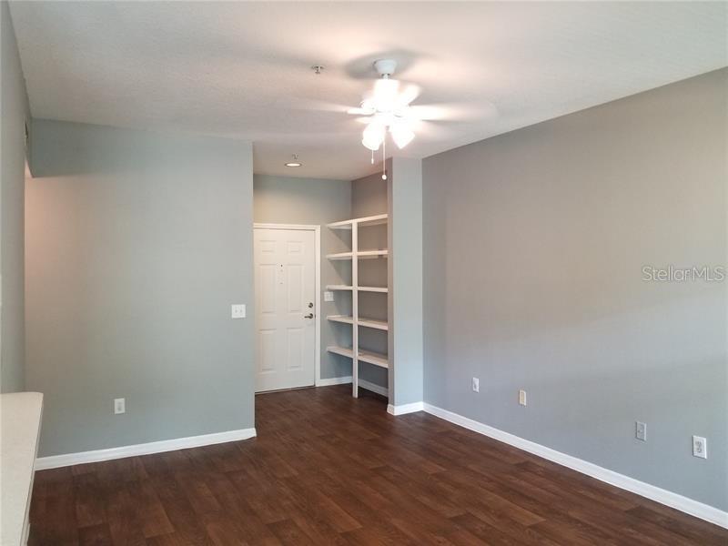 An empty room features gray walls, dark wood-look flooring, a ceiling fan, and built-in shelving — 1810 E PALM AVE UNIT 6204, TAMPA, FL