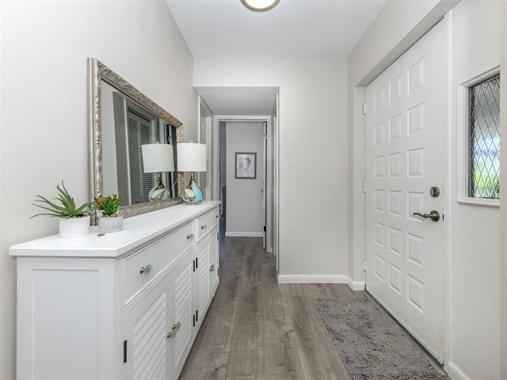 A white entryway features a wooden console table, a mirror, and gray wood-look flooring — 1712 LAKESIDE DRIVE UNIT 1712-B, VENICE, FL