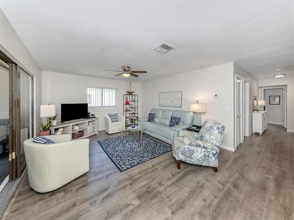 A living room features light wood-look flooring, a blue sofa, and a patterned accent chair — 1712 LAKESIDE DRIVE UNIT 1712-B, VENICE, FL