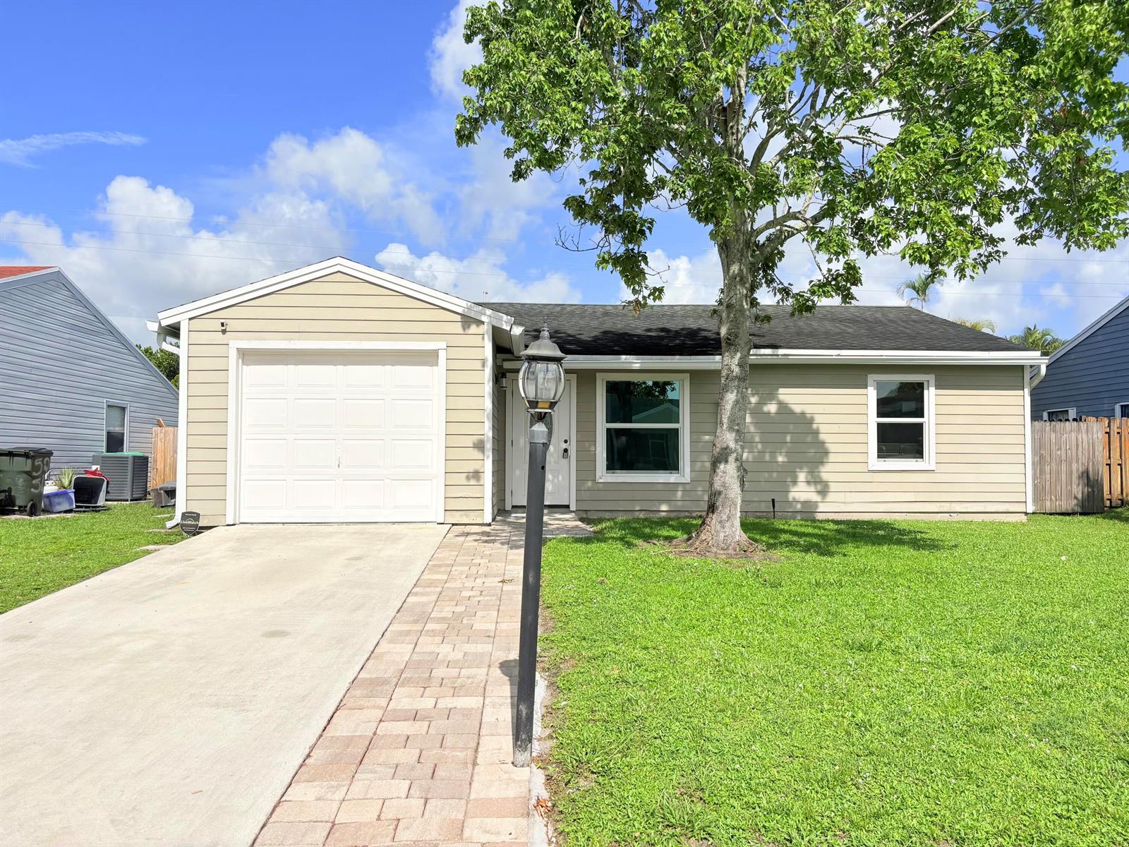 A single-story house with tan siding, a white garage door, and a paved walkway — 5258 Canal Circle W, Lake Worth FL 33467, LAKE WORTH, FL