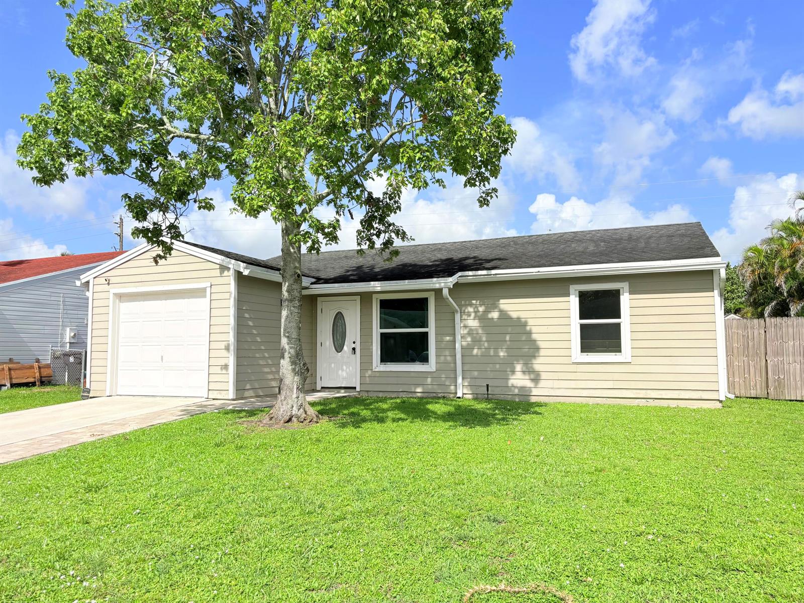 A single-story house with tan siding, a white garage door, and a large front tree — 5258 Canal Circle W, Lake Worth FL 33467, LAKE WORTH, FL