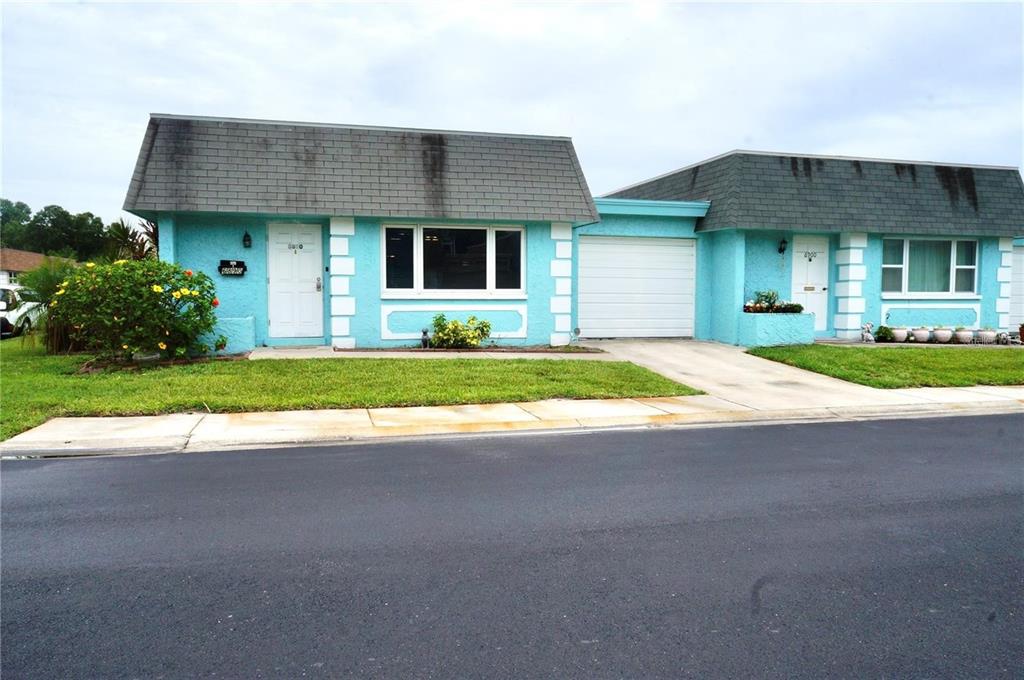 A bright blue duplex with a gray mansard roof and a shared concrete driveway — 6890 VERSAILLES N UNIT 10, PINELLAS PARK, FL