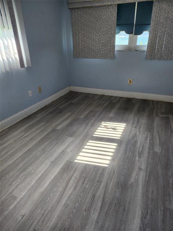 An empty bedroom features light blue walls, grey wood-look flooring, and windows with blinds — 6890 VERSAILLES N UNIT 10, PINELLAS PARK, FL