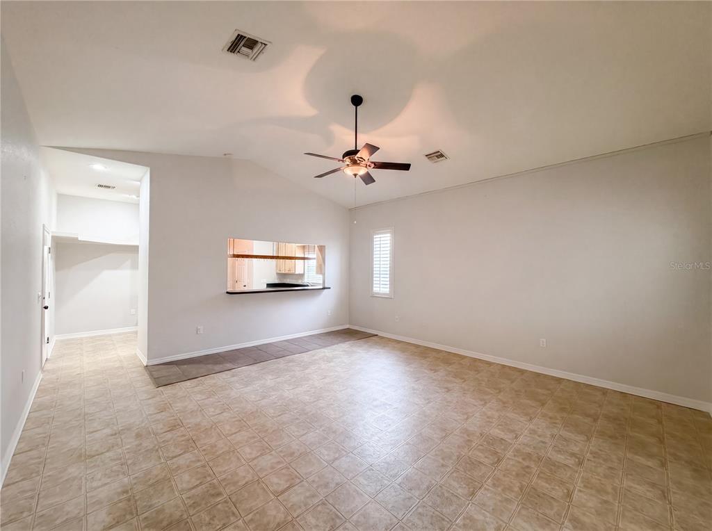 An empty living room features tile flooring, a vaulted ceiling with a fan, and a pass-through — 376 TRAVELERS DRIVE, POLK CITY, FL